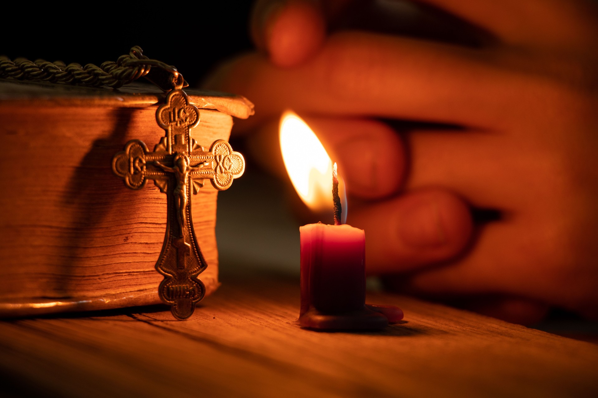 A woman holds a cross near a candle and a bible in the dark, a woman prays, praying, faith and religion